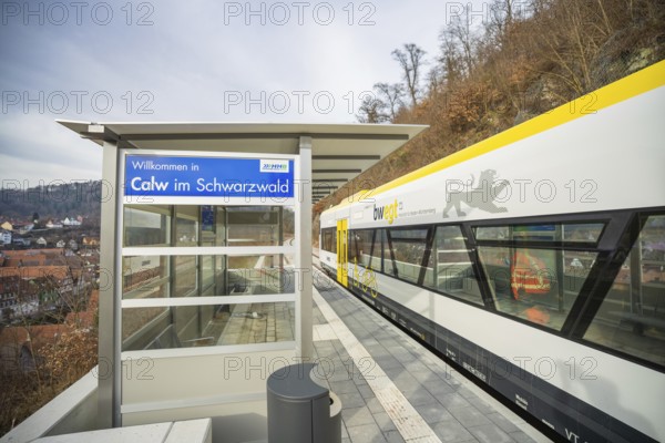 A modern train station in Calw with an outbound train surrounded by wooded hills, taking the