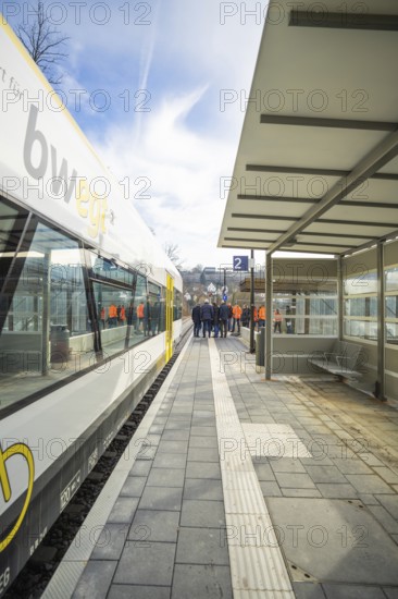 A train station with a stopping train and a group of people moving on the platform, acceptance of