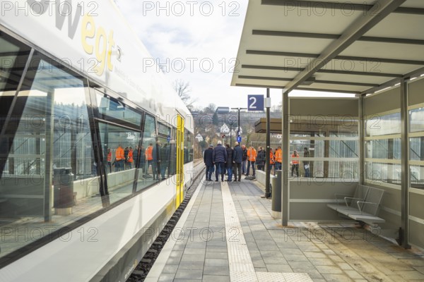 People standing in a group on a platform next to a train at a bus stop, the Hermann Hessebahn ride,