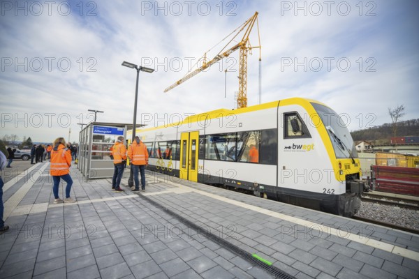 People standing on the platform next to a train and a construction crane in cloudy skies, the
