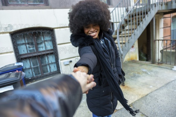 Young black woman smiling, looking back, and holding a hand, guiding through a city street in