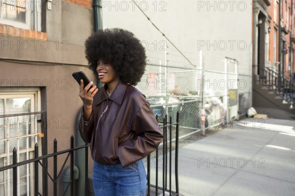 Young african american woman with afro hairstyle laughing while sending an audio message on her