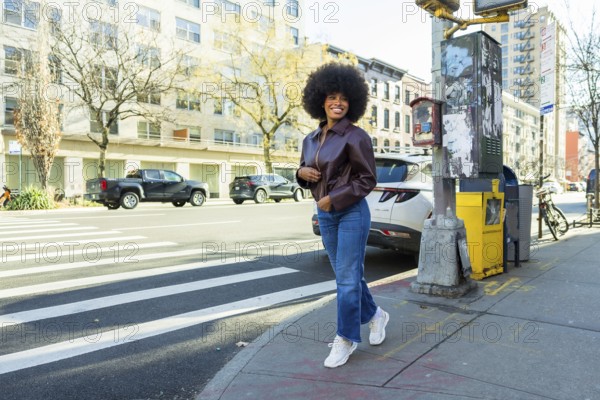Young black woman smiling confidently, walking briskly on a manhattan city street, wearing a