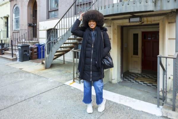 Joyful black woman with afro smiling confidently on a manhattan brownstone street in casual winter