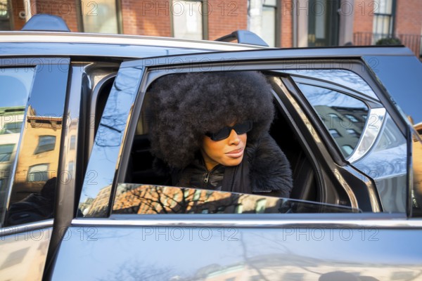 Elegant black woman wearing large sunglasses and an afro hairstyle, looking out of a car window