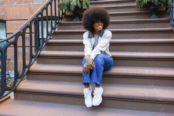 Young black woman sitting on brownstone steps in harlem, smiling and relaxed in casual street