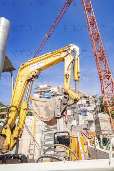 Large yellow excavator on a construction site surrounded by construction cranes, carpentry, new