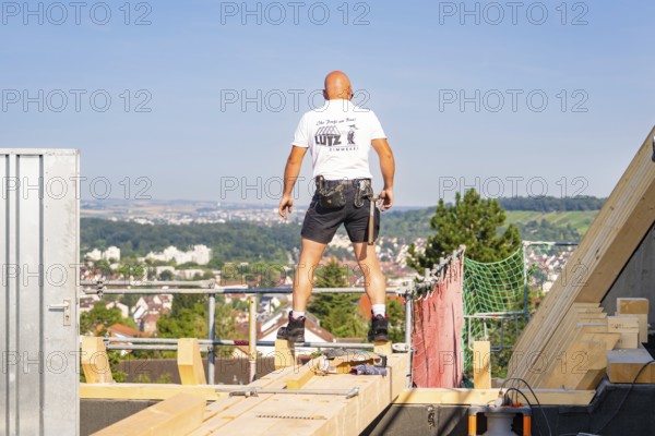 A construction worker on a roof with a view of the urban landscape under bright sky, carpentry, new