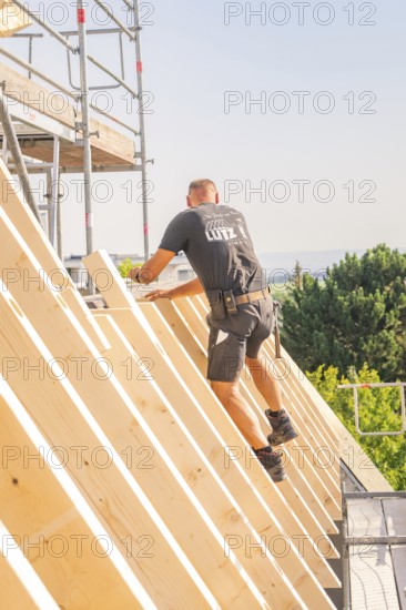 A construction worker climbs up a wooden structure on scaffolding against a blue sky, carpentry,
