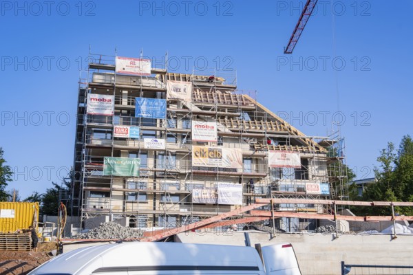 Multi-storey building with scaffolding and banners under clear, sunny sky, carpentry, new building,