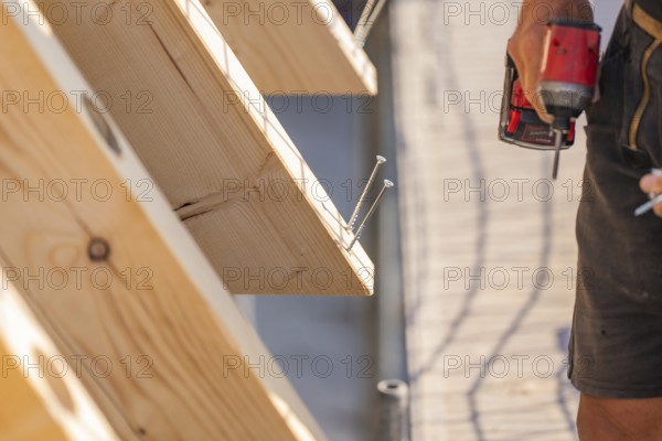 Worker holding drill next to wooden board with screws already screwed in, carpentry, new building,