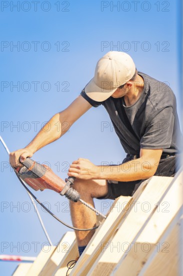 Construction worker working with a drill on a roof in sunny weather, carpentry, new building,