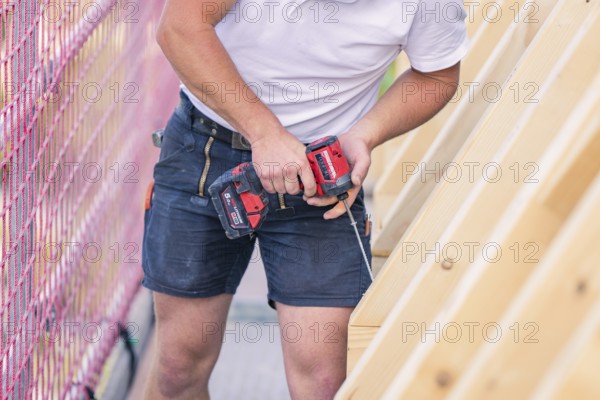 A construction worker uses a screwdriver to work on a wooden structure next to a net, carpentry,