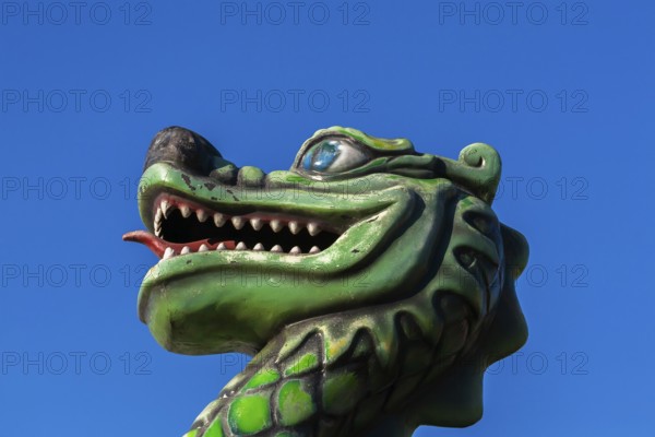 Green dragon with big teeth and long red tongue against blue sky background, Fun Show traveling