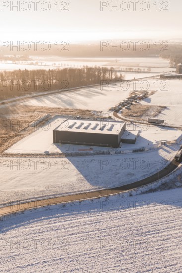 Warehouse in snowy landscape with surrounding roads and forests at sunset, Nagold, Calw district,
