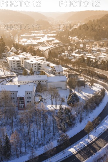 Residential building in a snowy urban landscape with roads and a bridge, surrounded by hills,