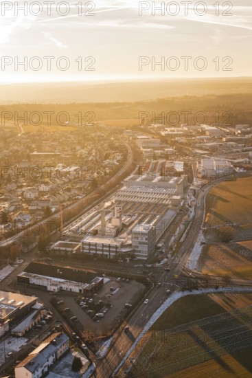 Industrial area and city in winter surroundings, illuminated by sunrise, fields and roads visible,