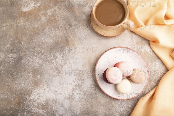 Macarons colourful cookies dessert, cup of coffee, on brown concrete background with orange linen