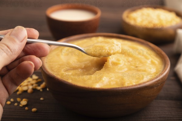 Pea cream soup, Puree, porridge in wooden bowl with hand on wooden background and linen textile.