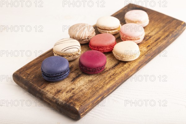 Macarons colourful cookies dessert on brown wooden cutting board on white wooden background, close