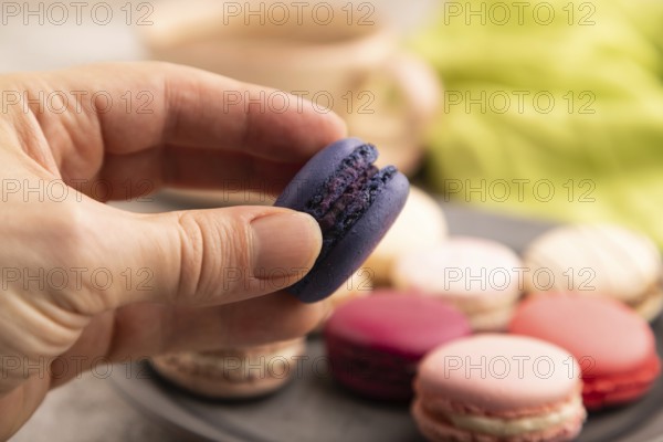 Macarons colourful cookies dessert with hand on brown concrete background with green linen textile,