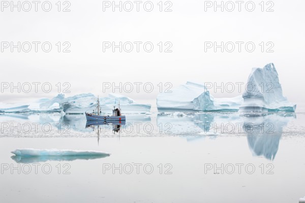 Fisherman's boat navigating near floating icebergs in the bay by Ataa village at sunset, Disko Bay,