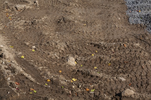 Deep tire tracks made by earth loader in light brown wet sand at construction site in early autumn,