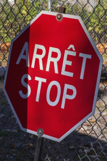 Close-up of bright red bilingual French arret and English stop sign with wire mesh fence in