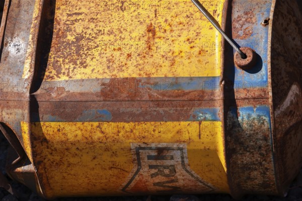 Close-up of discarded old rusted yellow and blue Irving Oil gas container laying on its side