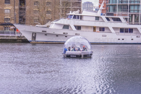 A boat with a glass dome on a body of water next to a large yacht in the harbor, London, England,