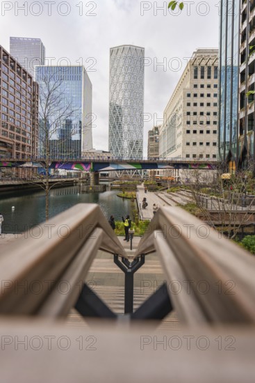 Modern buildings on a waterway with a bridge and sidewalks in the foreground, Canary Wharf, London,