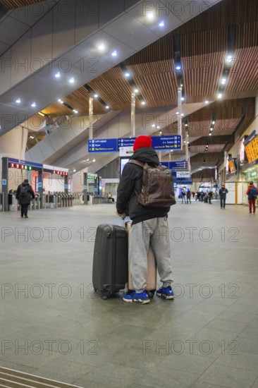 A person in a train station with luggage, modern interior and signpost in the background, London,
