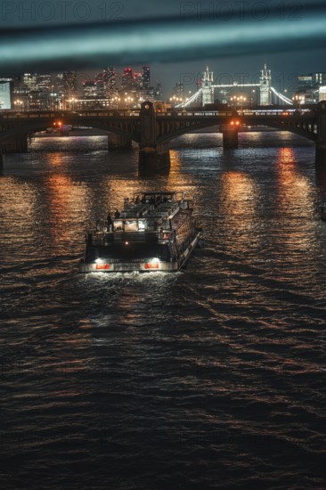 An illuminated boat on a river at night under a bright bridge in the city, London, England, Great