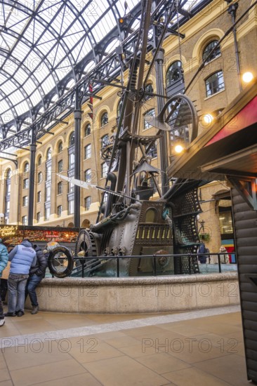 A large metal sculpture in a covered interior surrounded by people, The Navigators, London, United