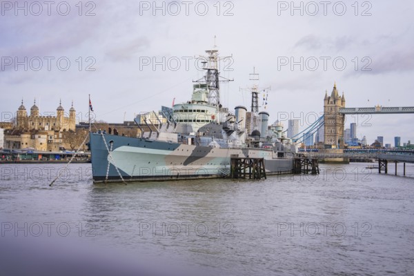 Large historic ship on the river in front of a bridge, with city skyline and towers on the horizon,