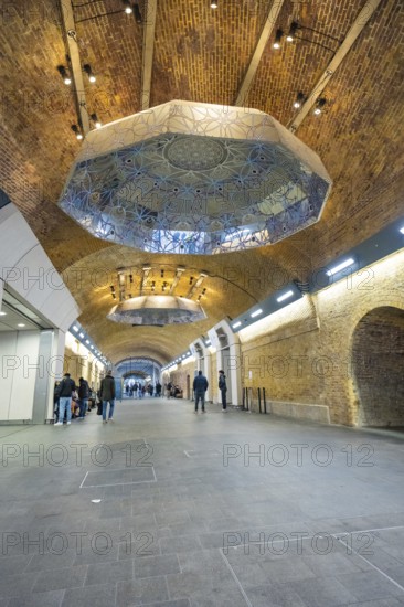 Long tunnel with decorative ceiling and people, warm lighting in an urban setting, London Bridge