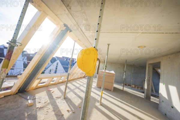 Construction site with yellow helmet on support, light concrete walls and wooden frame, carpentry,