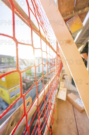 Red safety net on a railing allows sunlight to fall into a construction site, carpentry
