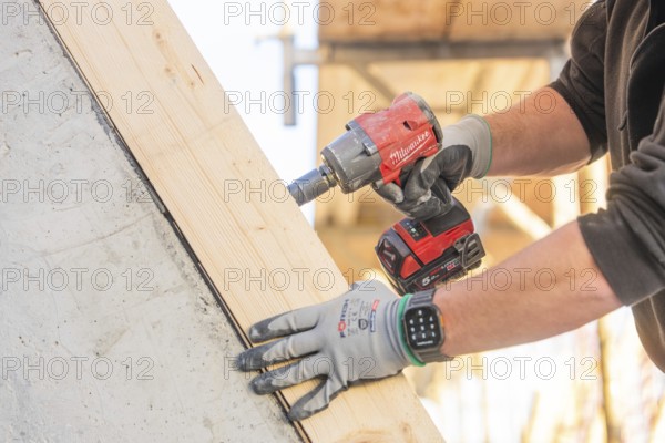 A worker with a cordless screwdriver fixing a piece of wood on a construction site, carpentry