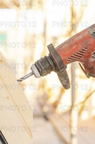 A drill drills into a slanted piece of wood, illuminated by sunlight, carpentry construction, roof