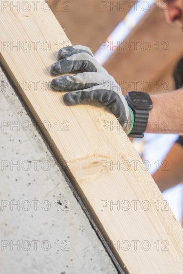 A gloved hand with a smartwatch holds a wooden board at a building, carpentry construction site,