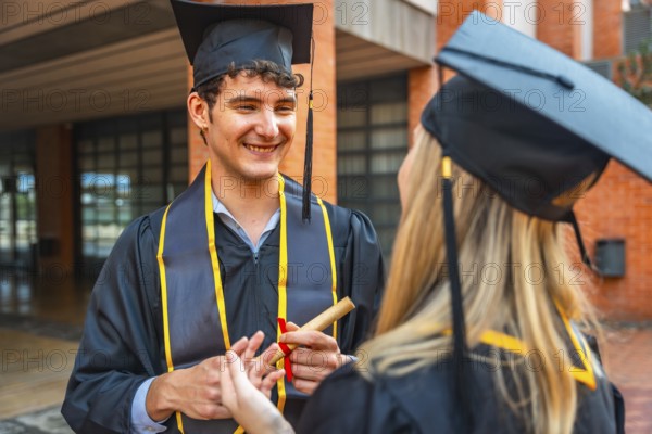 Graduating male student holding a rolled diploma, smiling and talking with a female classmate, both
