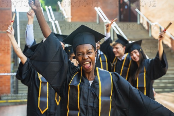 Smiling young woman posing with raised arms and holding a diploma while celebrating her academic
