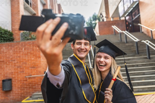 Graduating young man and woman wearing academic dress holding a diploma and filming a celebratory