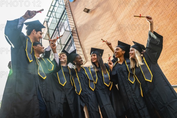 Diverse group of joyful young graduates in black caps and gowns celebrating on campus, holding