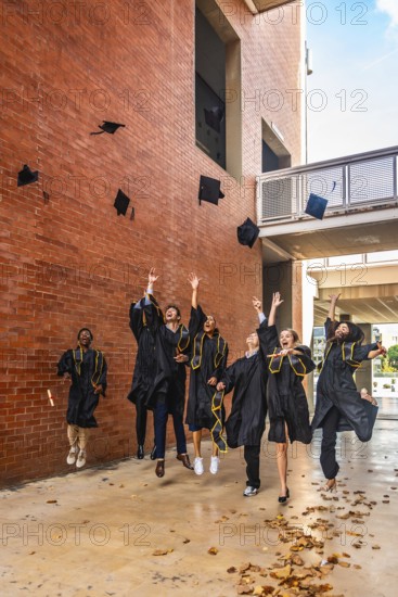 Group of happy diverse university graduates throwing their academic caps into the air and jumping