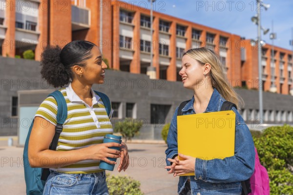 Two diverse female students walking on a university campus, smiling and engaged in conversation