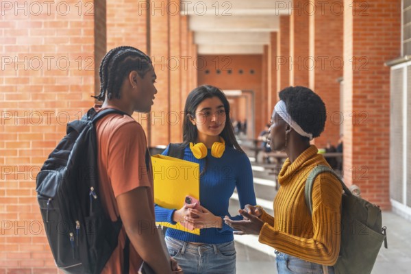 Three diverse university students are having a friendly conversation in a campus corridor,