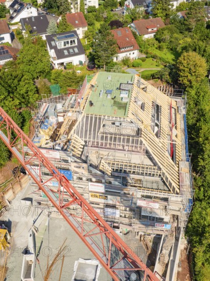Construction site with partially erected roof, crane and neighboring houses in a residential area,