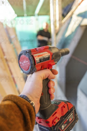 A worker holds a red electric screwdriver in a construction site situation, carpentry construction,